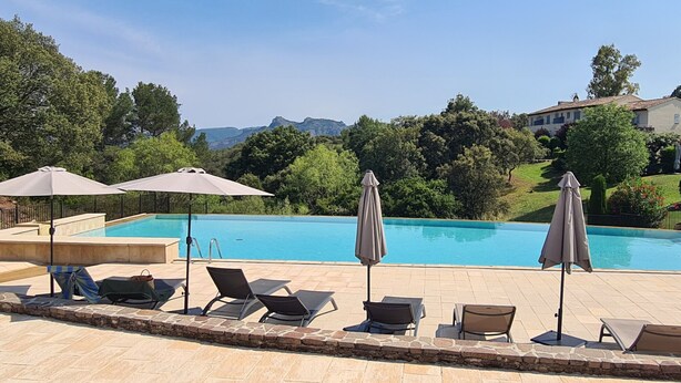 Una piscina con sillas de descanso y sombrillas, rodeada de vegetación y montañas.