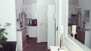Una cocina moderna con armarios blancos, un comedor con mesa de vidrio y un espejo que refleja la cocina.