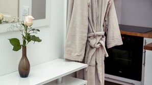 Un baño moderno con un tocador blanco, una bata colgada en un perchero y un florero con una rosa en la encimera.