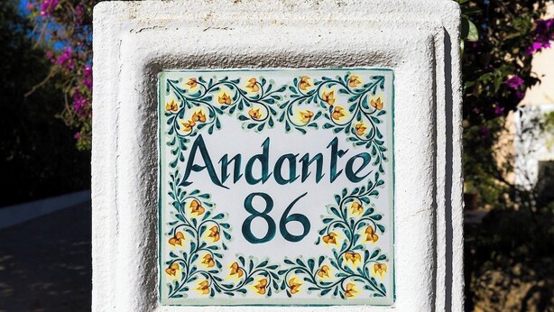 Een huisnummerbord met de naam 'Andante 86' omringd door een decoratieve bloemenrand.