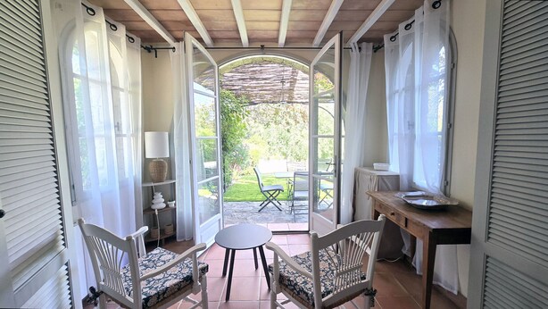 Ein Zimmer mit Blick auf einen Garten, ein Tisch mit Stühlen, eine Lampe und ein kleiner Tisch mit einer Schale.