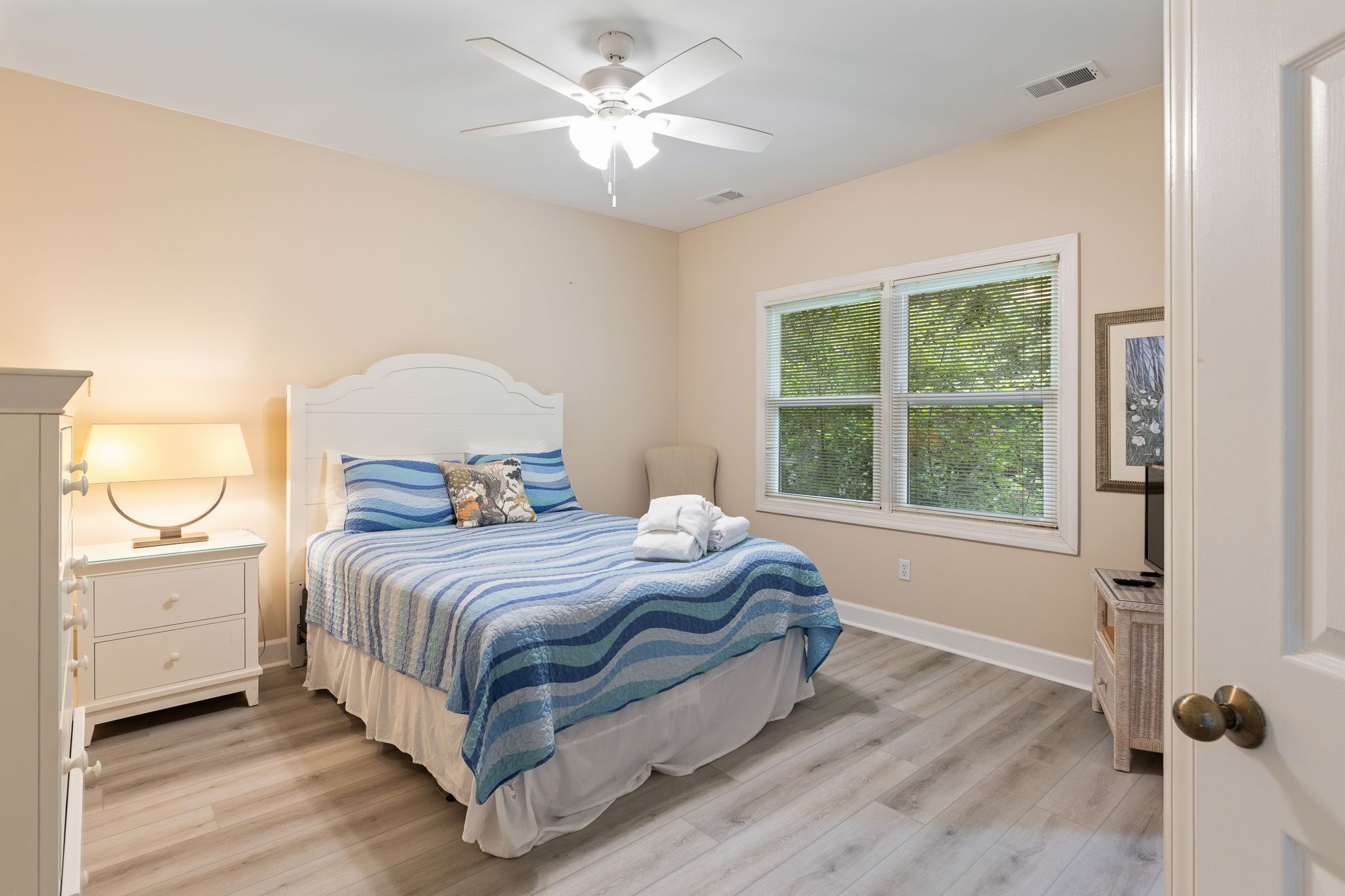 A bedroom with a bed, nightstand, lamp, ceiling fan, window, and a door.