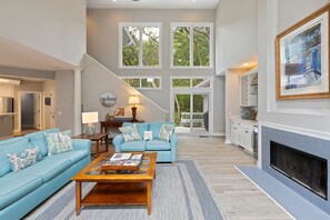 A spacious living room with a blue sofa, a wooden coffee table, and a fireplace. - Updated 4 Bedroom,  2nd Row Ocean Home | Private Pool & Spa | STR #026359 (Hilton Head Island)