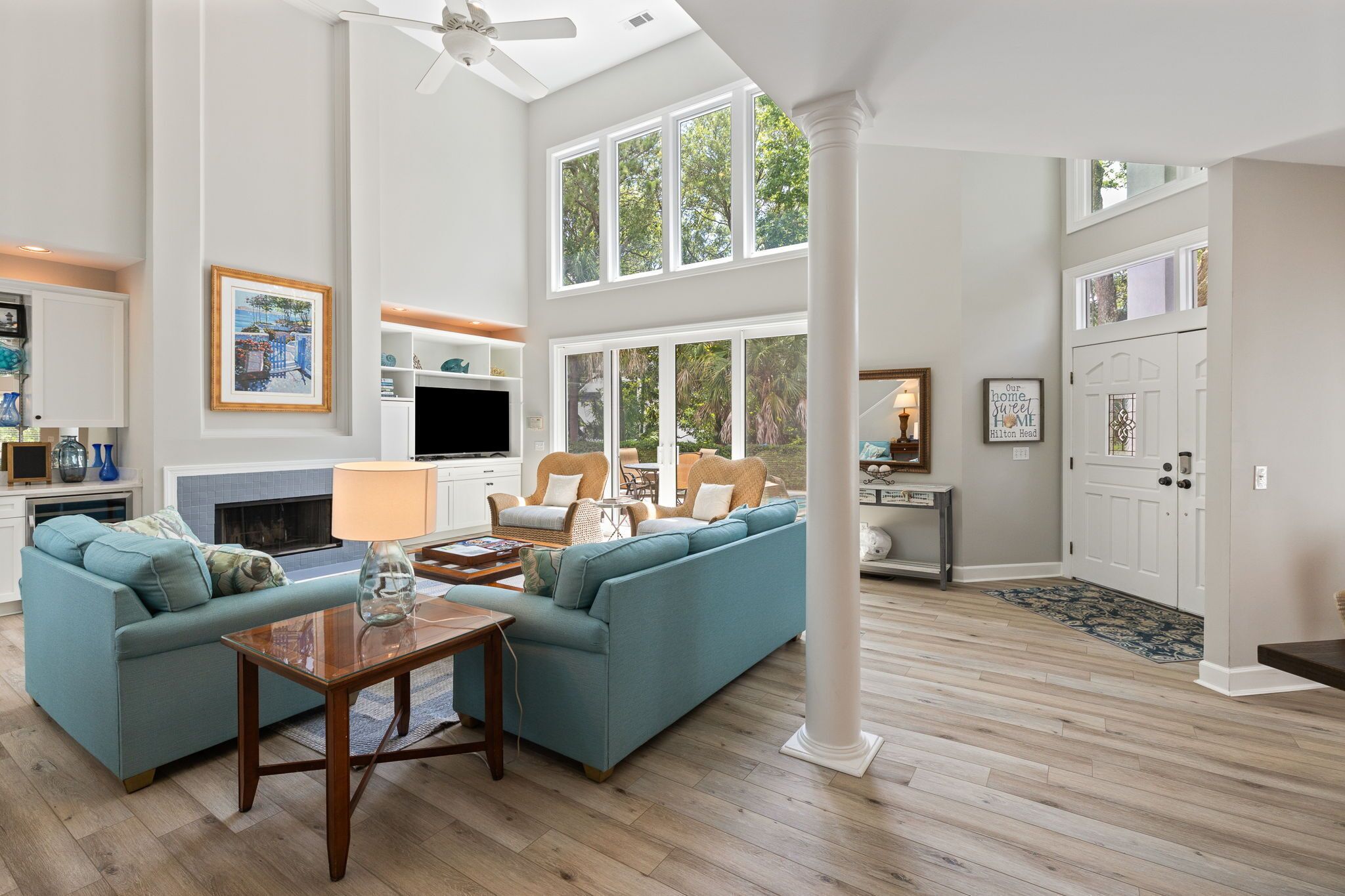 A spacious living room with a large blue sofa, a wooden coffee table, and a fireplace. There are multiple windows providing natural light and a view of the outdoors.
