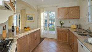 Une cuisine avec des meubles de rangement en bois, une cuisinière à gaz, un évier et une fenêtre avec des rideaux.