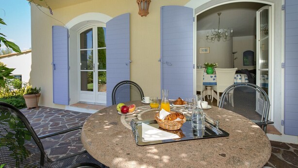 Une terrasse en pierre avec une table ronde mise pour le petit-déjeuner, comprenant des fruits, des viennoiseries et des boissons.