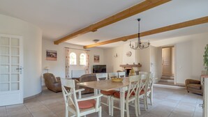 A dining area with a wooden table and chairs, a chandelier, and a kitchen in the background. - 5 BEDROOM VILLA WITH PRIVATE POOL AND GARDEN (N°359) (La Motte)