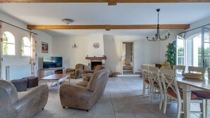 A spacious living room with a fireplace, a dining area with wooden chairs, and a television. - 5 BEDROOM VILLA WITH PRIVATE POOL AND GARDEN (N°359) (La Motte)