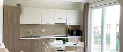 A modern apartment with a dining area, kitchenette, and a large window providing a view of the outside.