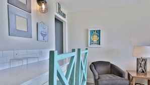 A modern living room with a grey armchair, a teal decorative gate, a framed artwork, and a lamp on a wooden side table. - 2nd Floor @ THE SUMMIT 1BR 1.5BA W/ BEACH CHAIRS INCLD. (Panama City Beach)