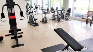 A gym with various exercise machines, a bench, and a window with a view of the outside. - Plaza Residence Jomtien Beach - Large Studio Condo (Pattaya)