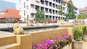 A hotel pool area with steps leading down to the water, surrounded by vibrant pink flowers and a statue of an elephant. - Plaza Residence Jomtien Beach - Large Studio Condo (Pattaya)