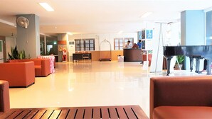 A spacious lobby with a reception desk, seating area, and a piano. - Plaza Residence Jomtien Beach - Large Studio Condo (Pattaya)