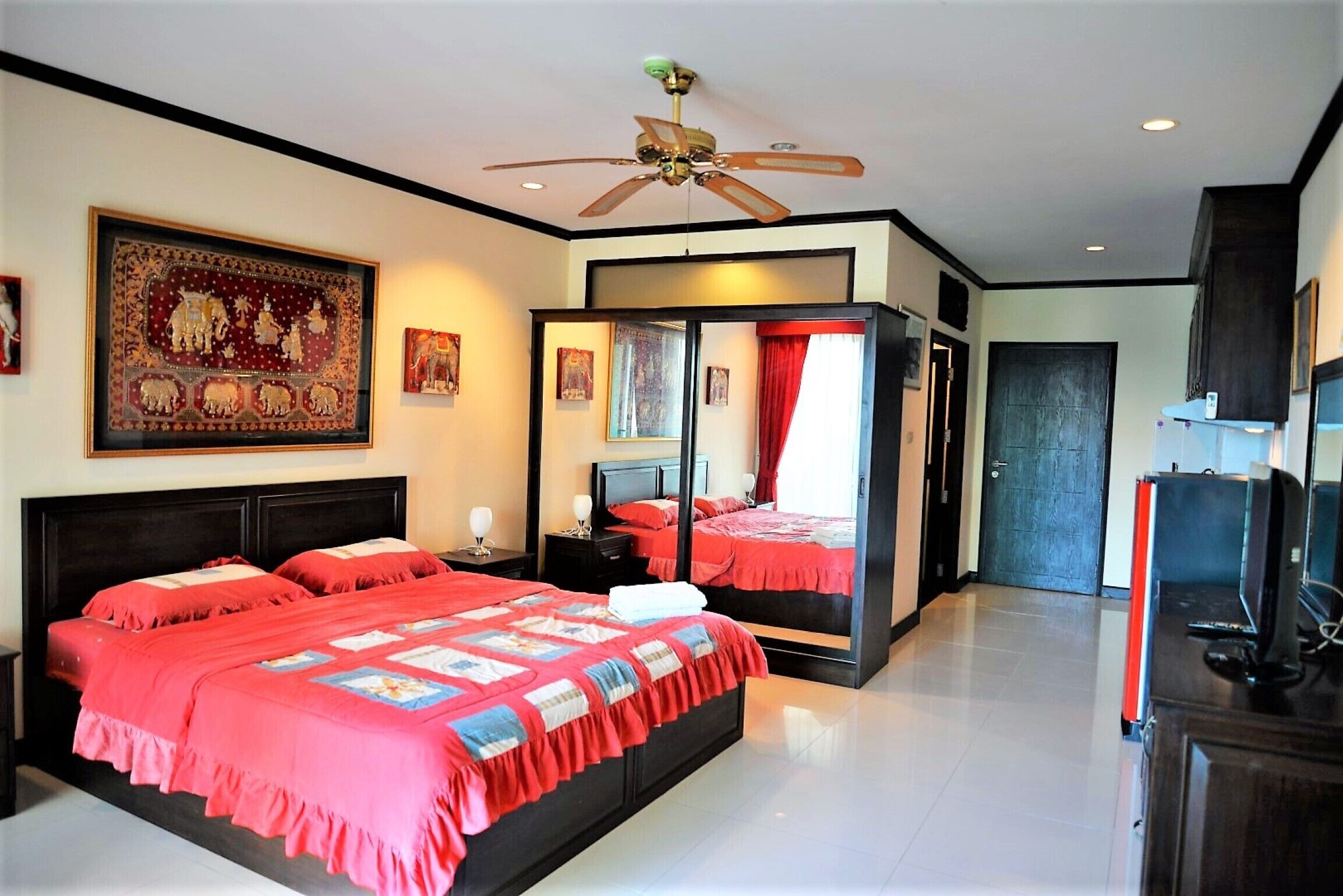 A bedroom with a large bed, a ceiling fan, and a mirror cabinet.