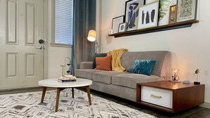 A living room with a grey sofa, a coffee table, a side table with a lamp, and a wall-mounted shelf with framed artwork. - Heart of Downtown - Bike Friendly - Ground Level (Bentonville)