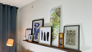 A living room with a sofa, a lamp, and a wall-mounted shelf displaying various framed artworks. - Heart of Downtown - Bike Friendly - Ground Level (Bentonville)