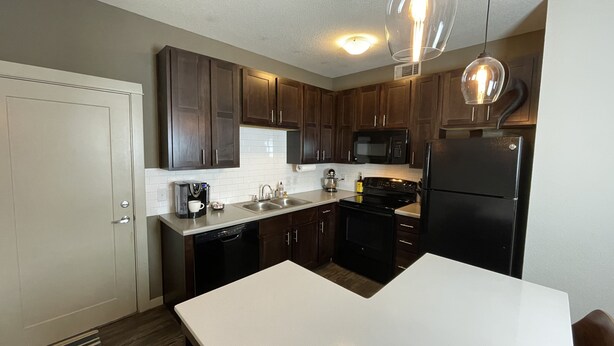 A modern kitchen with dark wooden cabinets, a white countertop, a black refrigerator, a microwave, and a coffee maker. - Heart of Downtown - Bike Friendly - Ground Level (Bentonville)
