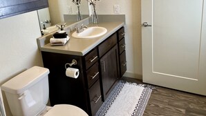 A modern bathroom with a white sink, dark wooden vanity, a toilet, and a black and white patterned rug. - Heart of Downtown - Bike Friendly - Ground Level (Bentonville)