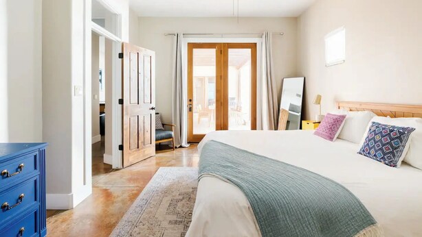 Ein Schlafzimmer mit Bett, Deckenventilator, Holztür, blauem Schminktisch und Blick ins Freie.