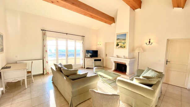 Una sala de estar con chimenea, televisor y un amplio ventanal con cortinas.