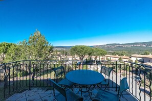 A balcony with a round table and chairs, overlooking a residential area with trees and houses.