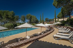 A poolside area with lounge chairs and umbrellas, surrounded by trees and buildings.