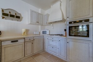 Una cocina con armarios blancos, lavavajillas Bosch, microondas, estufa a gas y horno.