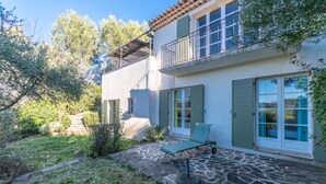 A two-story house with a stone patio, a lounge chair, and a balcony with metal railings. - 3 BEDROOM TOWNHOUSE WITH GARDEN (N°565) (La Motte)