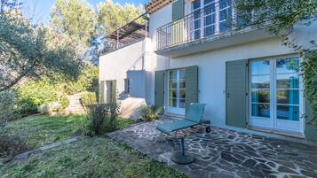 Une maison à deux étages dotée d’une terrasse en pierre, d’un fauteuil de relaxation et d’un balcon avec des balustrades en métal.