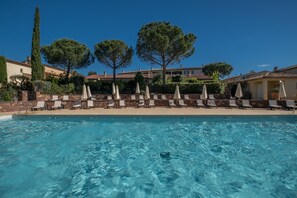 Ein Schwimmbecken mit Liegestühlen und Sonnenschirmen, umgeben von Bäumen und Gebäuden.