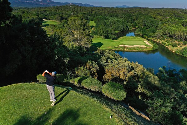 Ein Golfplatz mit Wasserfläche, Bäumen und hügeliger Landschaft.