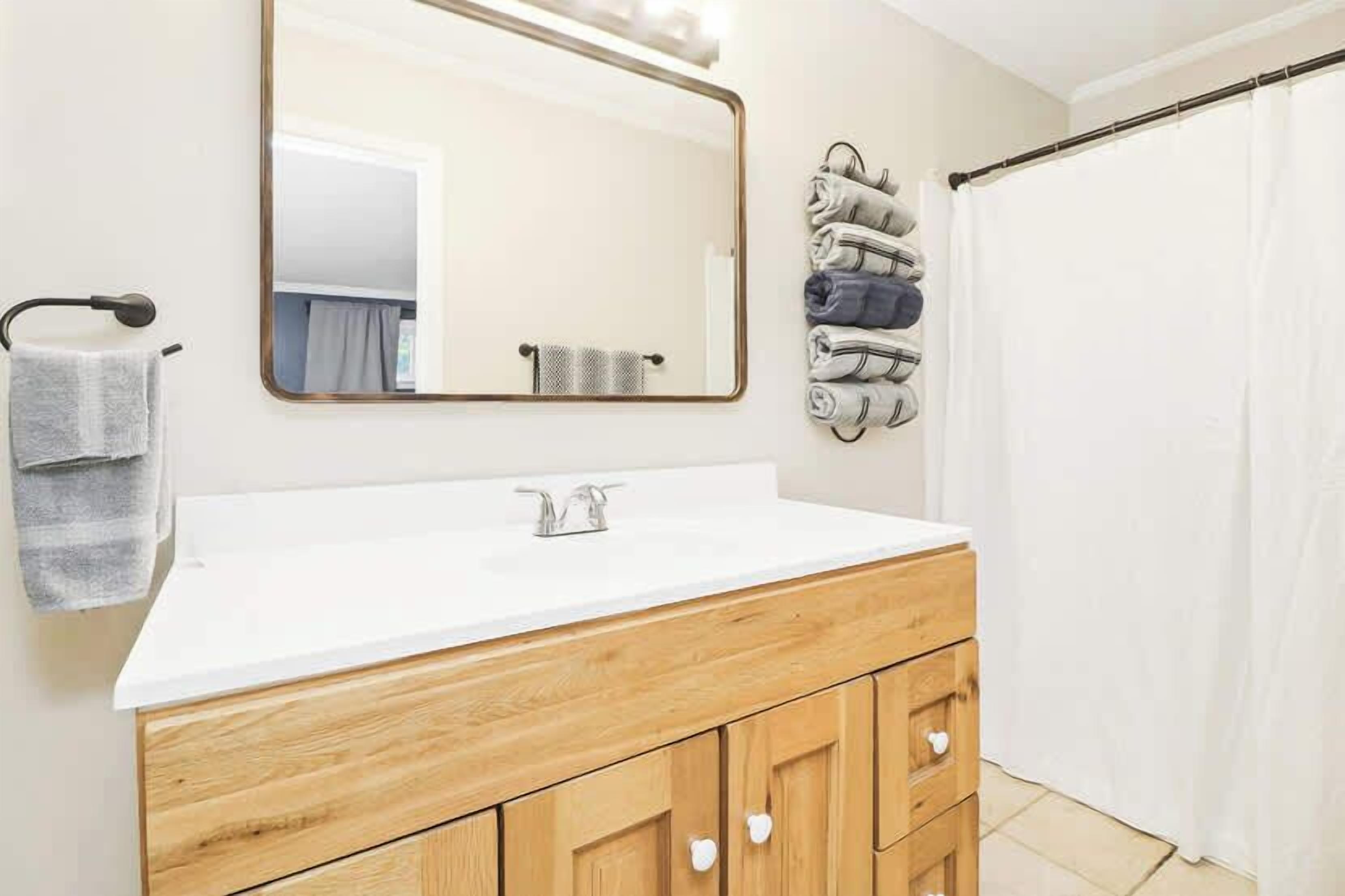 A bathroom with a white sink, wooden vanity, and a mirror.