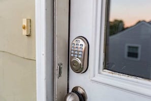 A door with a keypad lock, a door handle, and a window with a view of a house.