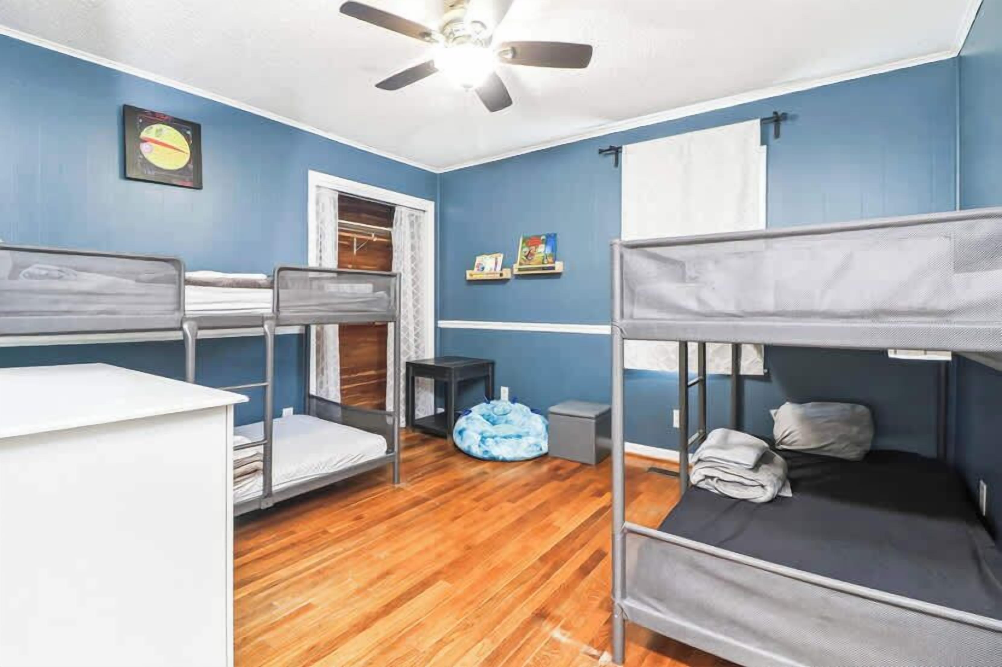 A dormitory room with bunk beds, a ceiling fan, a window, and a small desk.