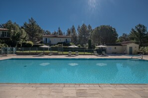 Une piscine avec une terrasse carrelée, entourée d’une clôture, et quelques parasols.