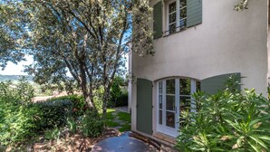 A patio with a round table and chairs, surrounded by lush greenery and a view of a hillside. - 3 BEDROOM TOWNHOUSE WITH GARDEN (N°329) (La Motte)