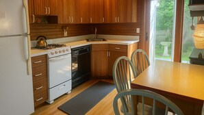 A kitchen with wooden cabinets, a stove, and a sink. There is a dining table with chairs.