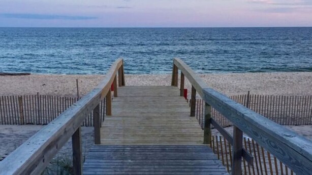 A wooden boardwalk leading to a beach with a wooden fence on either side.