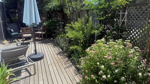 A wooden deck with outdoor furniture, a pergola, and a variety of plants and flowers.