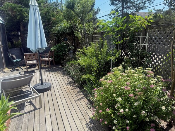 A wooden deck with outdoor furniture, a pergola, and a variety of plants and flowers.