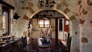 A rustic stone kitchen with wooden cabinets, a dining table with chairs, and a chandelier. - Palazzo Villa, World 5th Awarded Villa (Zakynthos)
