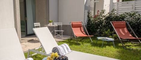 A modern outdoor seating area with white lounge chairs, a small table with a bowl of fruit, and a striped towel.