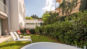 Area piscina moderna all'aperto con lettini, vasca idromassaggio e vegetazione lussureggiante.
