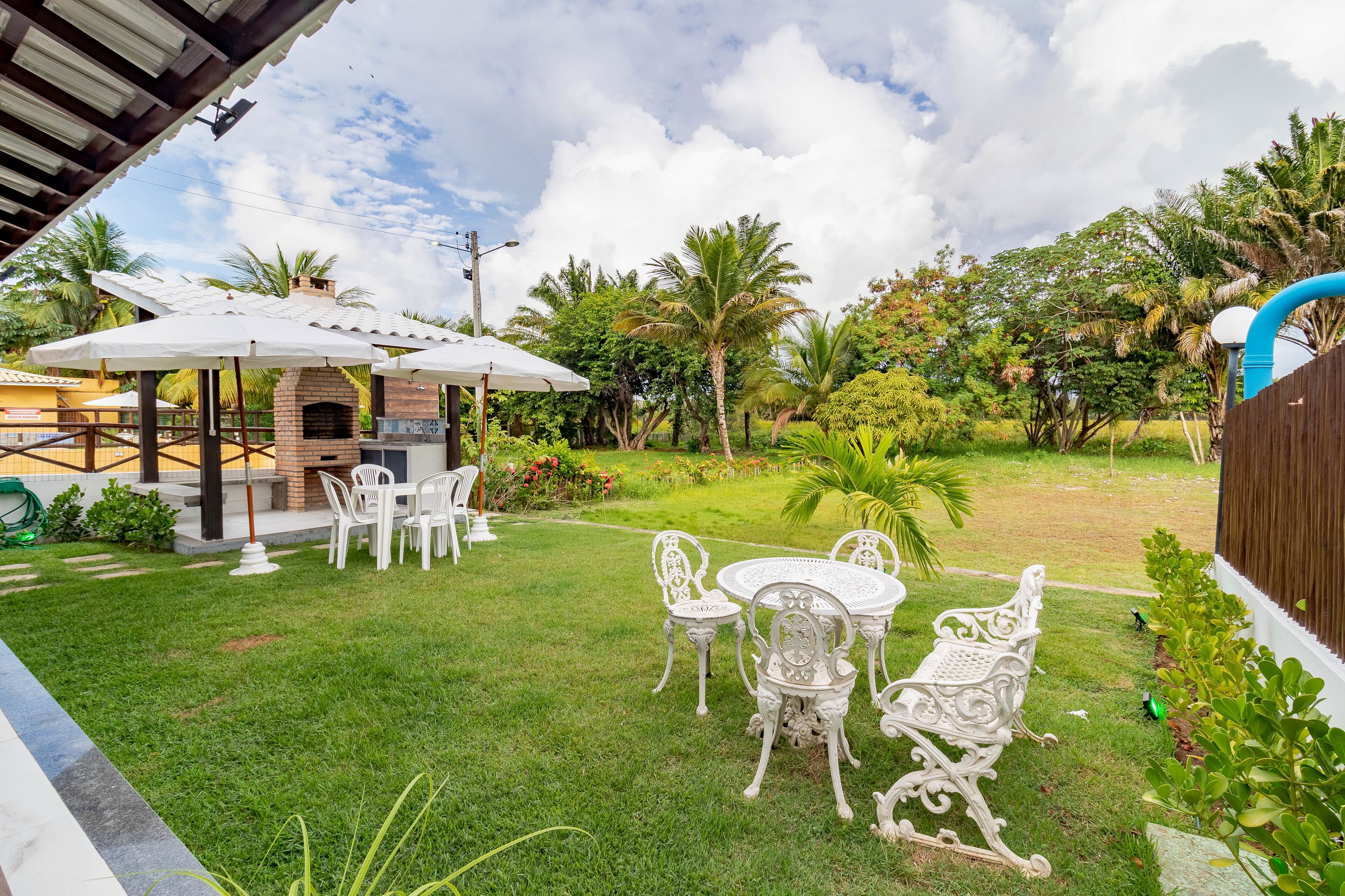 A patio area with a brick oven, white outdoor furniture, and lush greenery.