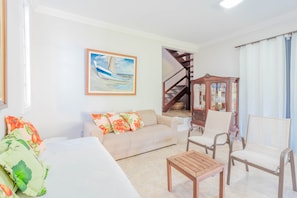 Una sala de estar con un sofá, sillas, una mesa de madera, un cuadro y una escalera.