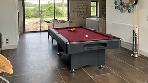 Ein Billardtisch in einem Raum mit Steinwänden, Blick durch eine Glastür und ein Kicker.
