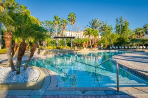 Una piscina con un borde pavimentado, palmeras y un edificio al fondo.