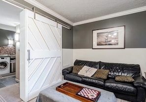 A living room with a black leather sofa, a wooden coffee table, a white sliding door, and a framed picture on the wall. - Presidential Suite Full Lower Apartment (Upper Marlboro)