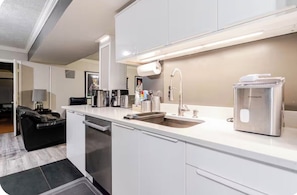 A modern kitchen with white cabinetry, a stainless steel coffee maker, and a built-in dishwasher.