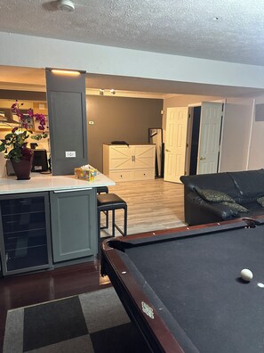 Une table de billard dans une pièce comprenant un coin cuisine, une table à manger et une porte donnant sur une autre pièce.